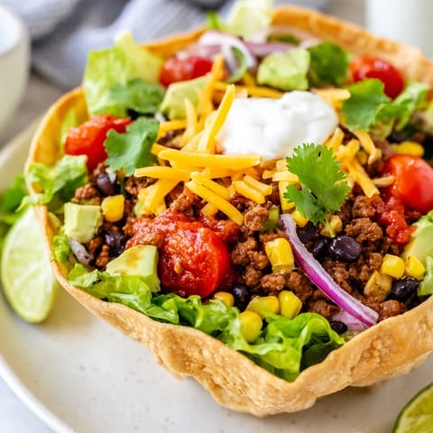 Golden-brown tortilla bowls brimming with Taco Salad, a hearty meal with seasoned beef and creamy sauces.