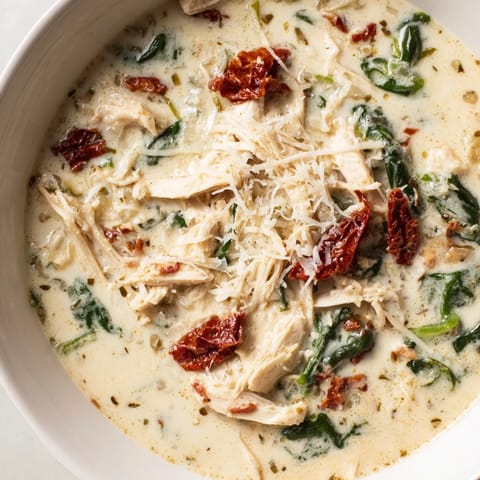 Steaming Creamy Tuscan Chicken Soup in a white pot, featuring shredded chicken and vibrant sun-dried tomatoes.