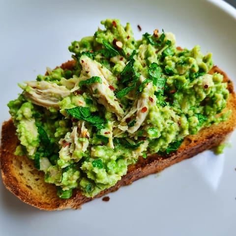 Savory Smashed Pea & Chicken Toast on a white plate, with a lemon wedge and a glass of crisp white wine.