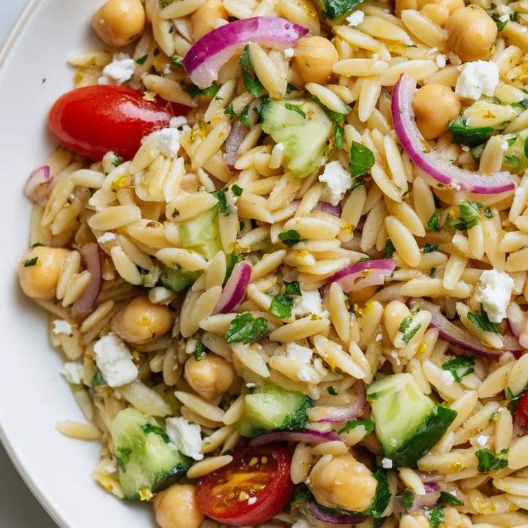 Vibrant Lemony Chickpea Orzo Salad ready to serve on a picnic blanket, with crumbled feta and fresh mint garnish for a refreshing light meal.