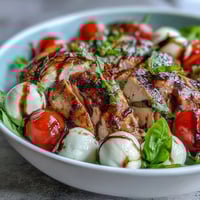 Grilled chicken slices, mozzarella, and ripe tomatoes on greens for a fresh Caprese Chicken Bowl.